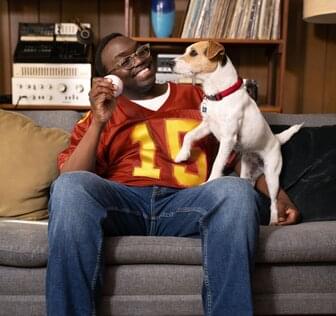 sports fan and his dog sitting on living room couch playing with ball